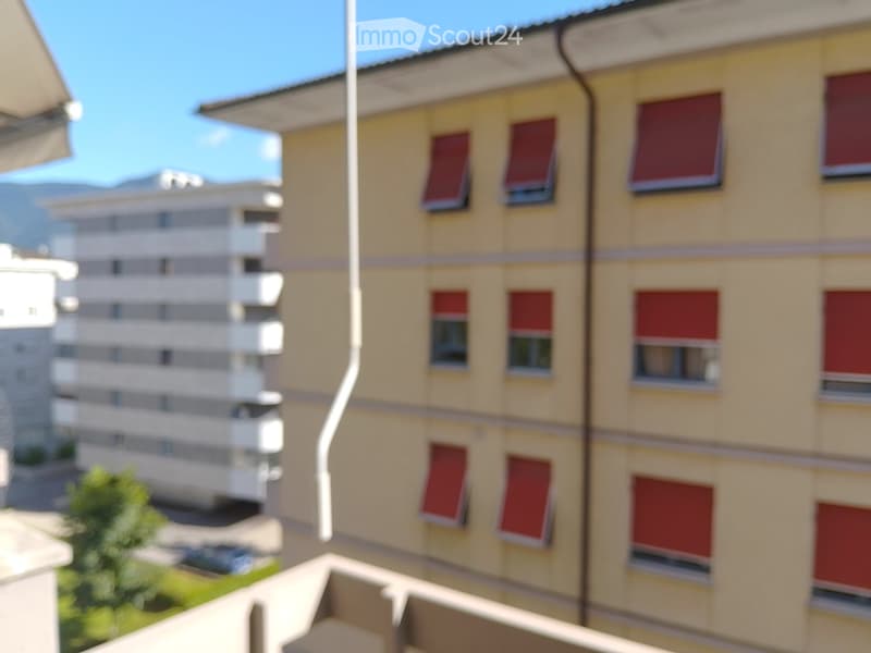 Balcony overlooking a multi-story residential building with red shutters and a clear blue sky.