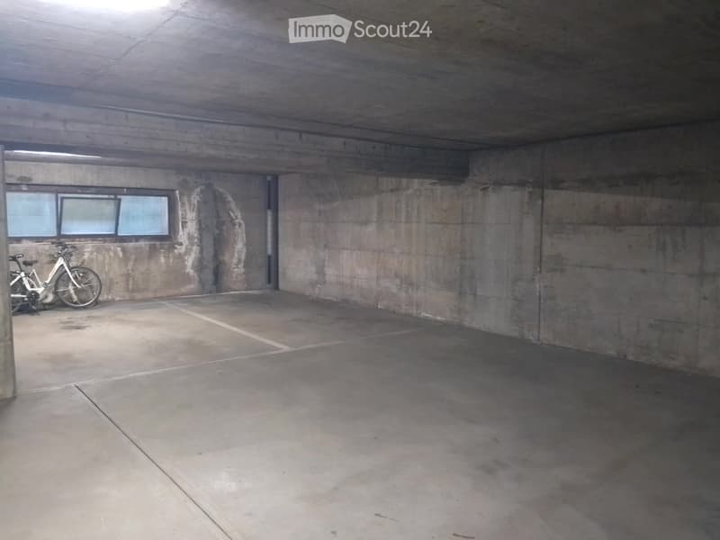 Underground parking area with concrete walls and floor, two bicycles parked against the wall, small window at the far end.