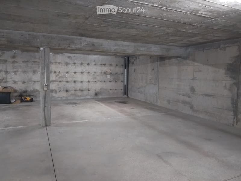 Empty concrete-walled garage with a single door and a small storage area in the corner.