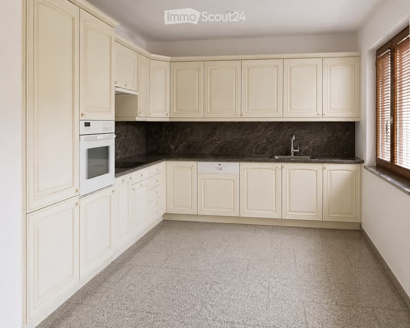 Empty kitchen with white cabinets, granite countertop, and tiled floor.