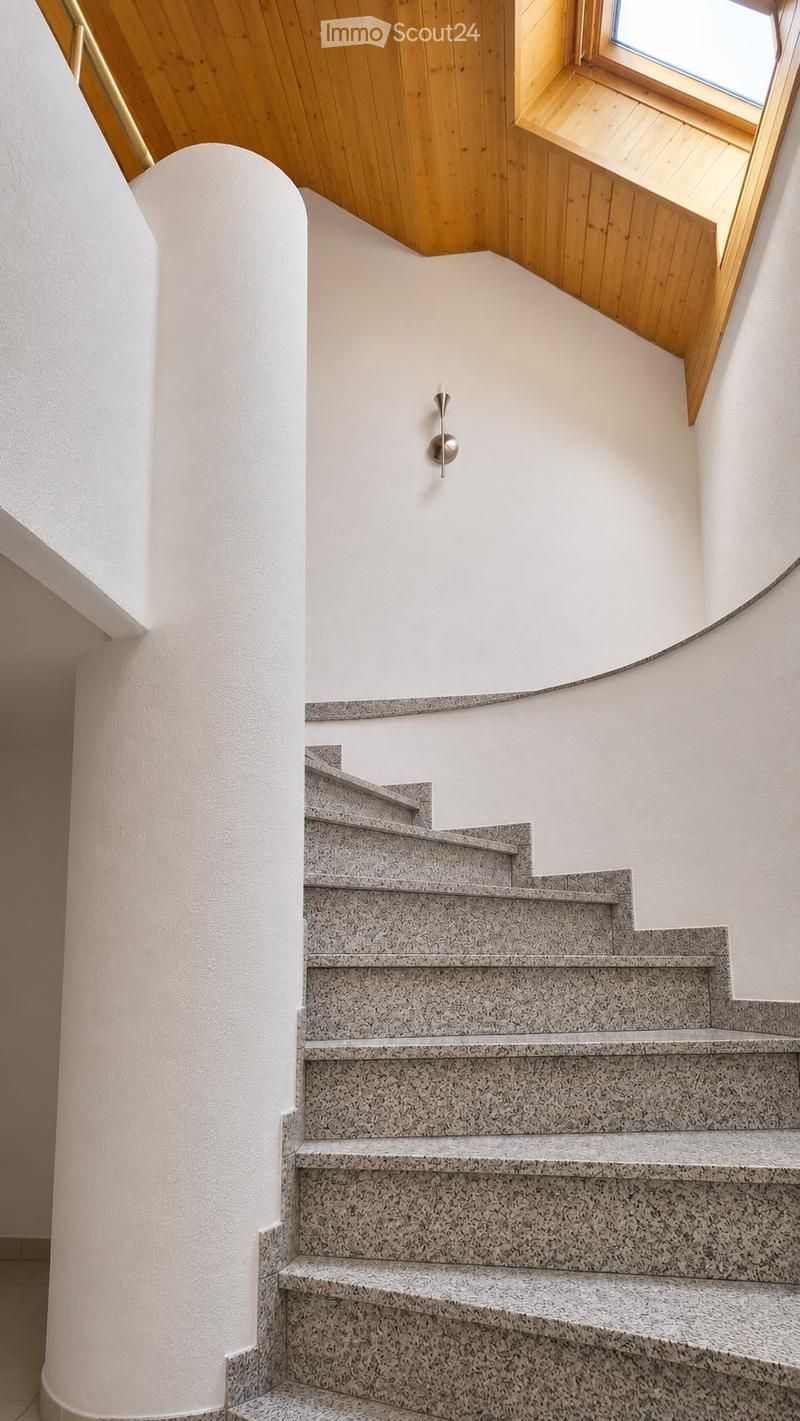 Spiral staircase with granite steps and a modern, curved design, featuring a sleek wall-mounted light fixture and a wooden ceiling with a skylight window.