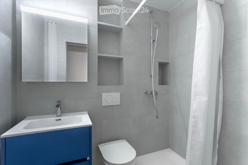Modern bathroom with grey tiles, blue vanity, white sink, mirror, toilet, and shower with a glass curtain.