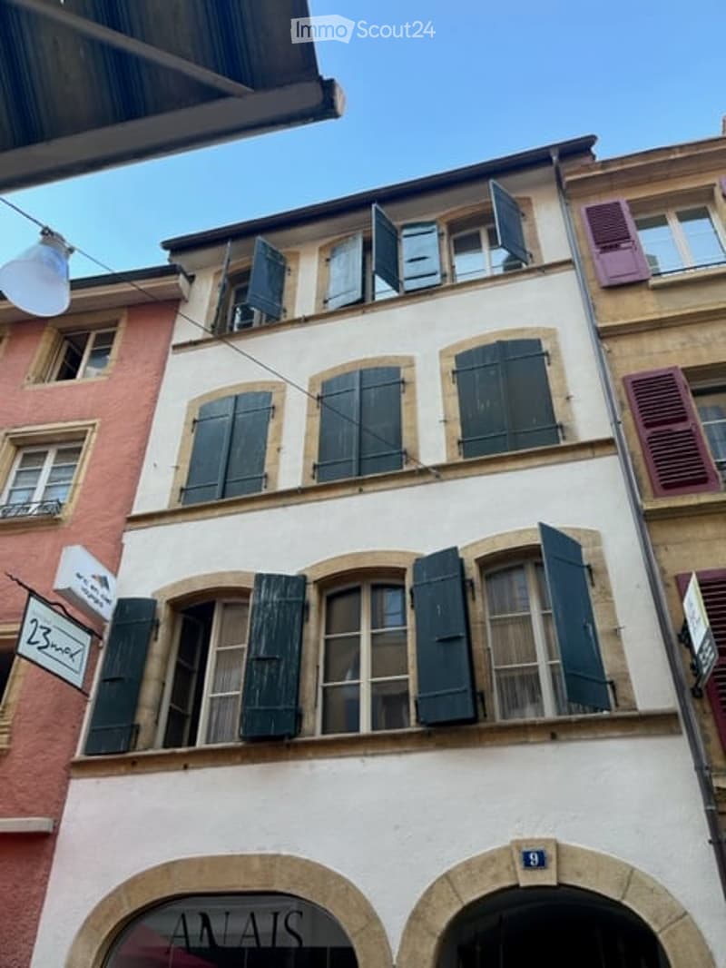 Classic European building with multiple stories, green shutters, arched ground-floor windows, and a sign reading "ANATS" above the entrance.