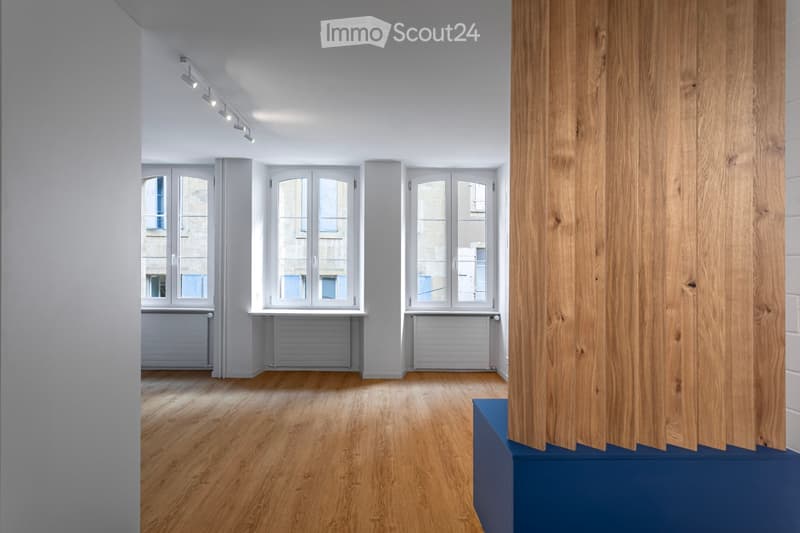 Empty room with wooden flooring, white walls, large windows, and radiators. No furniture or equipment present.