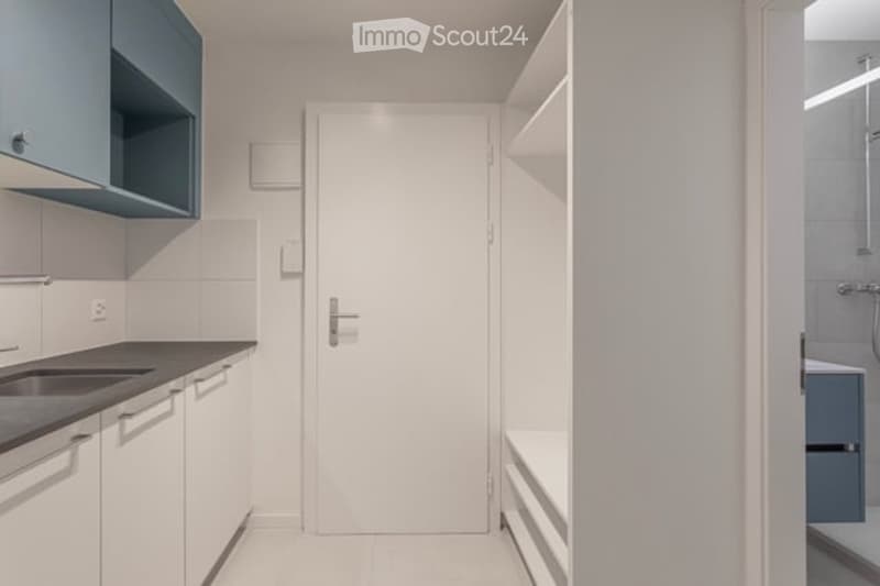 Modern, minimalist kitchen with white cabinets, a sink, and a door leading to another room.