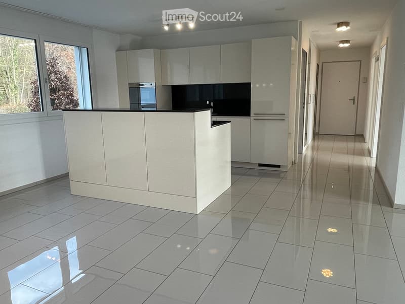 Modern kitchen with white cabinets, a central island, and a built-in oven. The space features large windows and a polished tile floor.