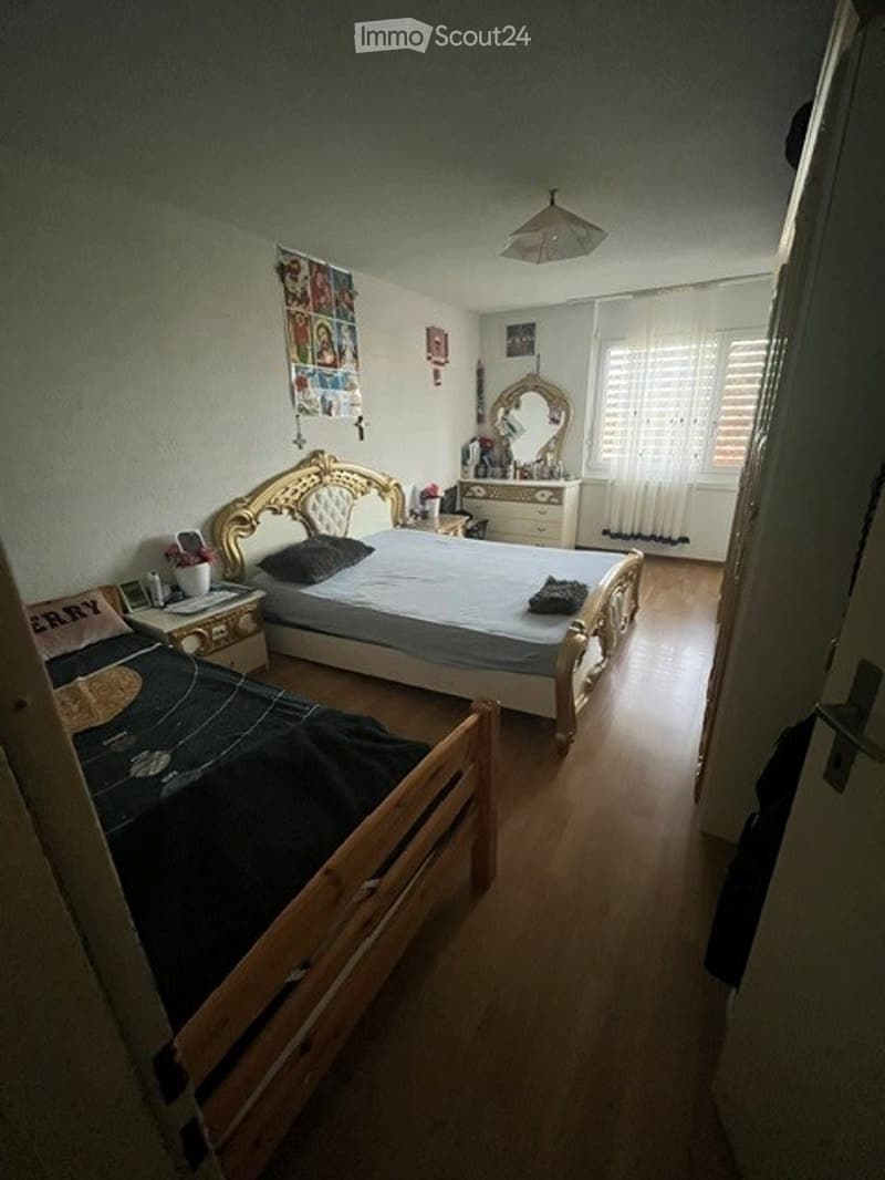Cozy bedroom with two beds, one with a decorative headboard, a nightstand, a dresser with a mirror, and a lamp.