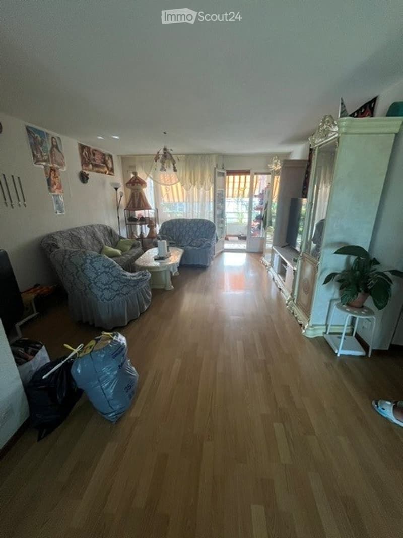Living room with wooden flooring, two sofas, coffee table, armchair, floor lamp, mirror, cabinet, and a potted plant.
