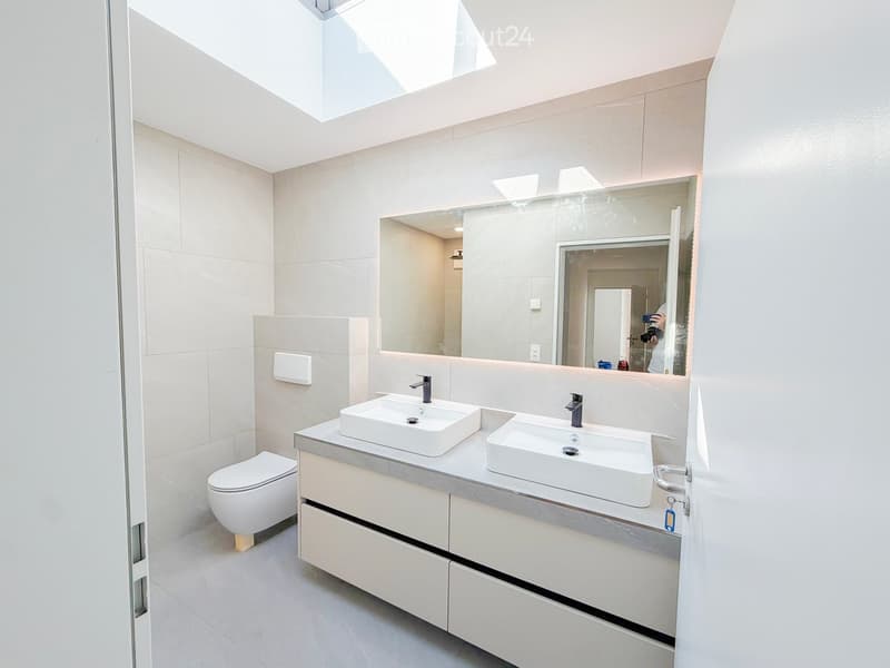 Modern bathroom with two white sinks, a toilet, a large mirror, and built-in cabinets.