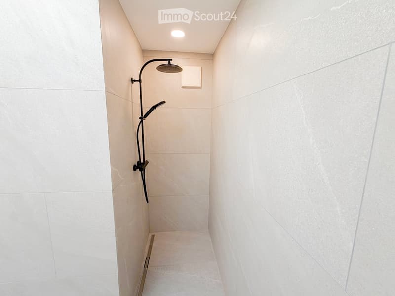 Modern shower area with white tiled walls and floor, featuring a sleek black showerhead and handheld sprayer.