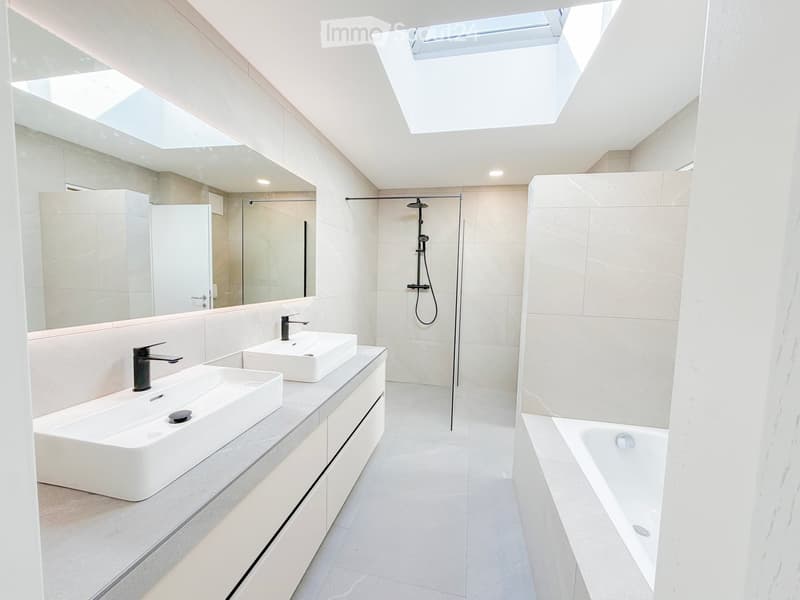 Modern bathroom with two white sinks, a bathtub, a shower, and large mirrors. The space features light-colored tiles and sleek fixtures.