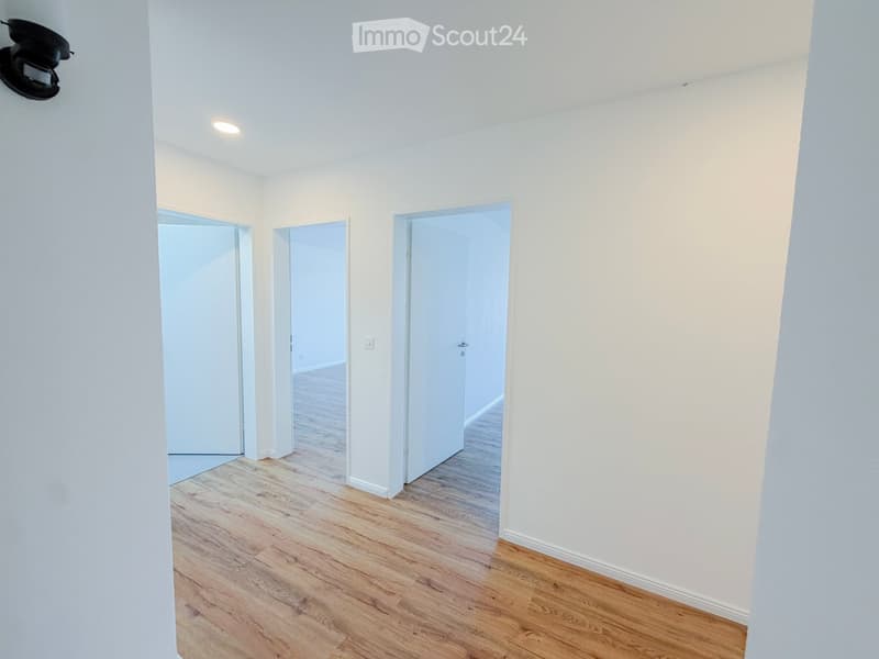 Empty room with light wooden flooring, white walls, and three open doors leading to other spaces.