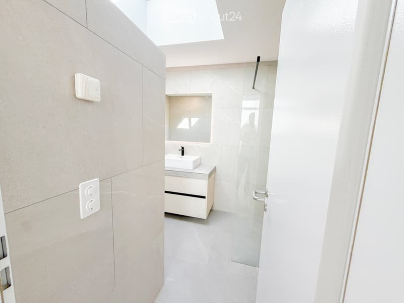 Modern bathroom with a white sink, mirror, and cabinet, featuring a glass shower enclosure and sleek tile walls.