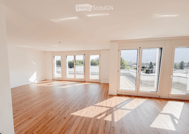 Empty room with wooden flooring, large windows, and sliding doors leading to a balcony with a scenic view.