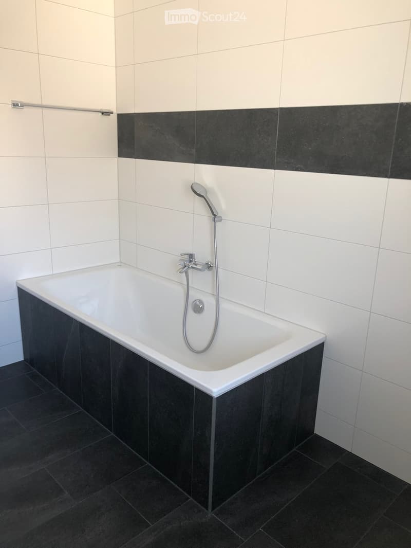 Modern bathroom with a white bathtub, black tiled walls and floor, and a handheld showerhead attached to the wall.