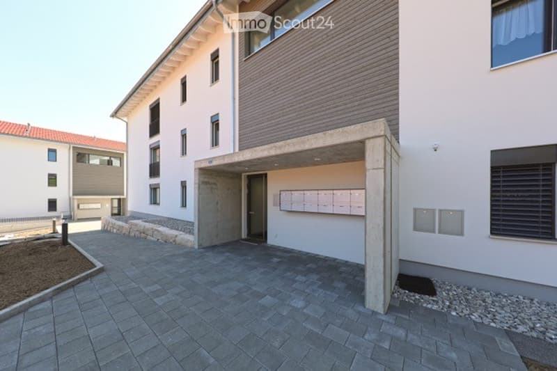 Modern multi-story building with a raised ground floor entrance, concrete facade, and tiled pavement.