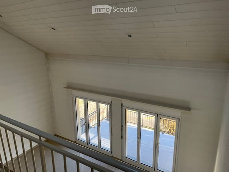 Spacious hallway with wooden ceiling, white walls, and large glass doors leading to a balcony or terrace area.
