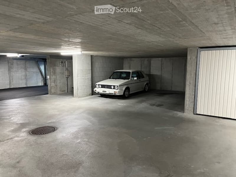 Underground garage with a single parked car, concrete walls and ceiling, and a metal door on the right side.