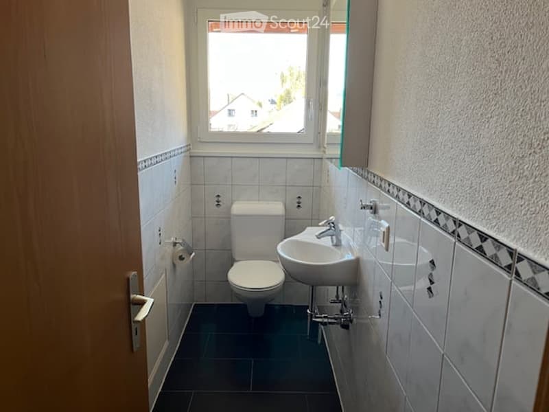 Small bathroom with white tiles, a toilet, a sink with a faucet, a mirror, and a window letting in natural light.