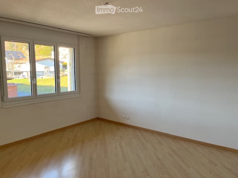 Empty room with wooden flooring, white walls, and large windows offering a view of the outdoors.