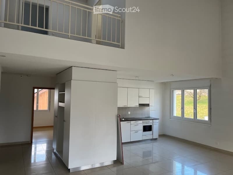 Open-plan unfurnished space with a modern kitchen area, white cabinets, and a balcony overlooking the area.
