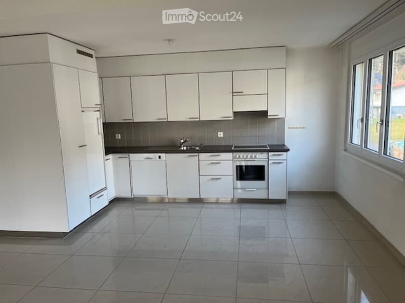 Modern, minimalist kitchen with white cabinets, stainless steel appliances, and tiled flooring.