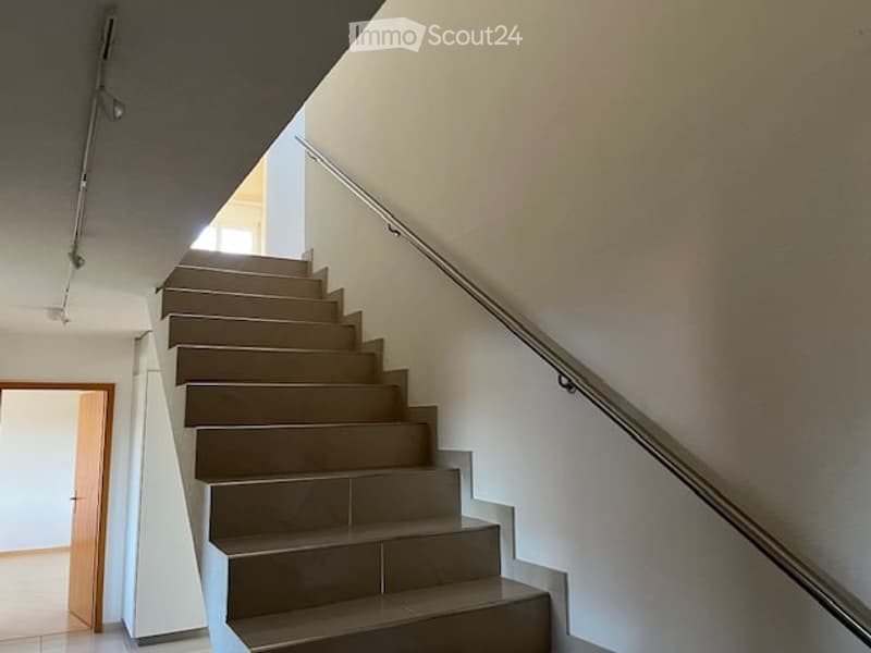 Modern staircase with beige tiled steps and a metal handrail, leading to an open doorway at the end.