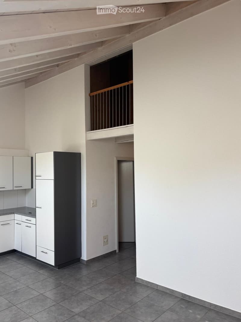 Modern kitchen with white cabinets, stainless steel appliances, and a tiled floor. An open staircase leads to an upper level.