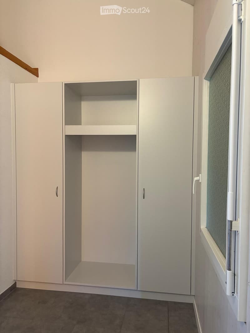 Empty hallway with white built-in cabinets and a window with frosted glass. The floor is tiled, and the walls are painted light beige.
