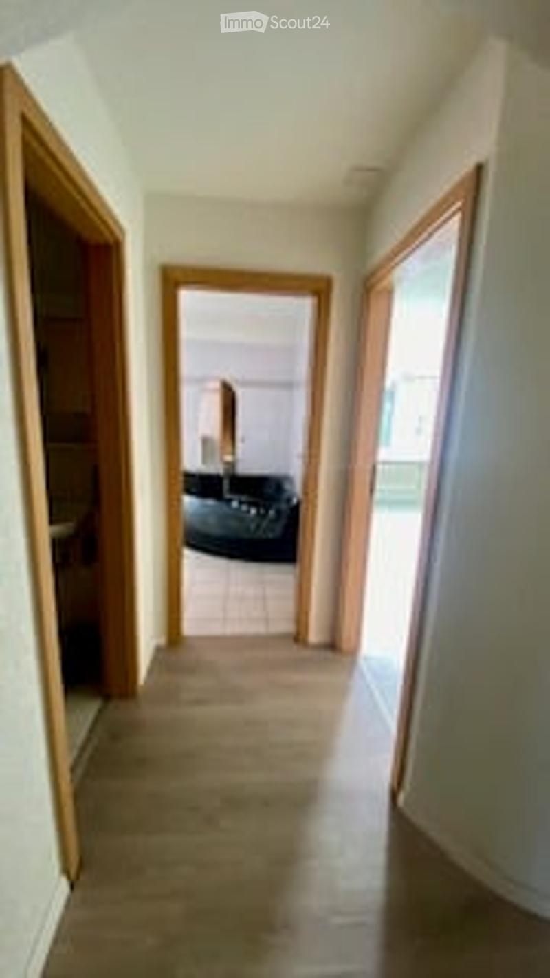 A narrow hallway with wooden doors on both sides, leading to a room with visible furniture.