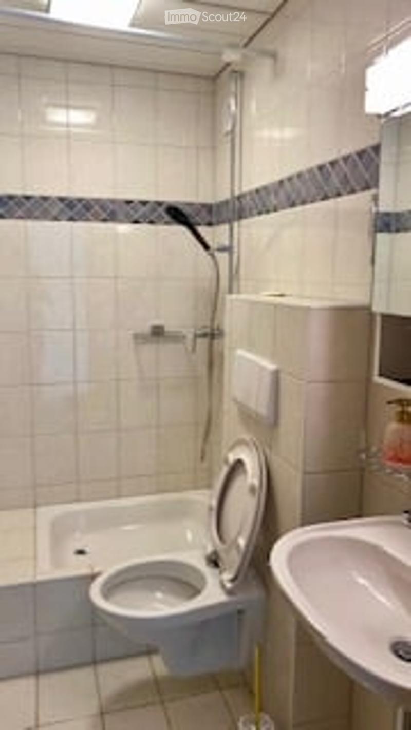 A small bathroom with a toilet, sink, bathtub, and a mirror above the sink. The walls are tiled in beige with a decorative border near the top.