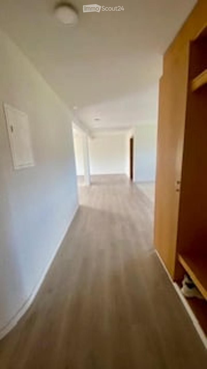 Empty hallway with light wooden flooring, white walls, and a built-in wooden cabinet on the right side.