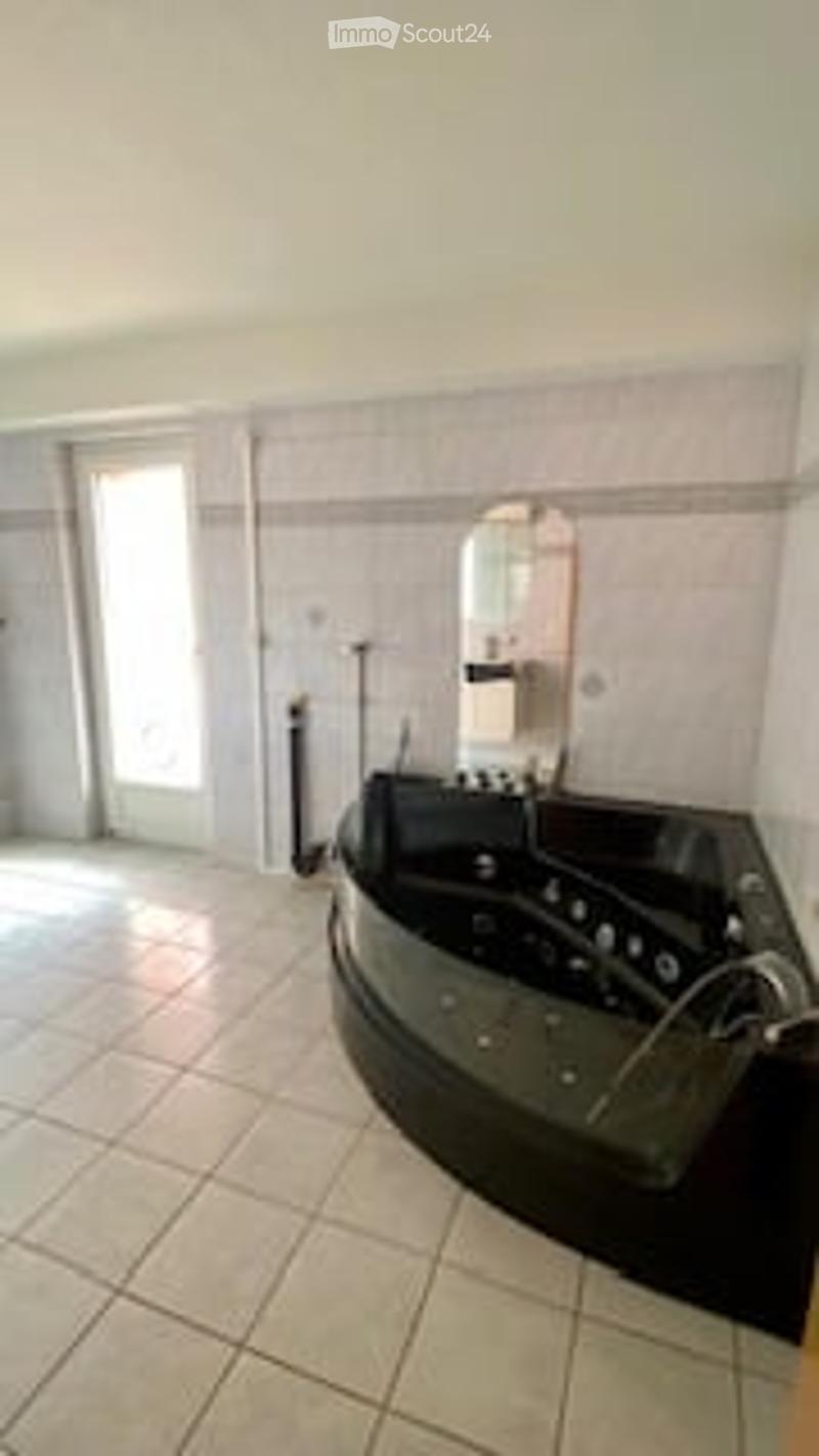 Modern bathroom with a large black bathtub, a large mirror, and a tiled floor.