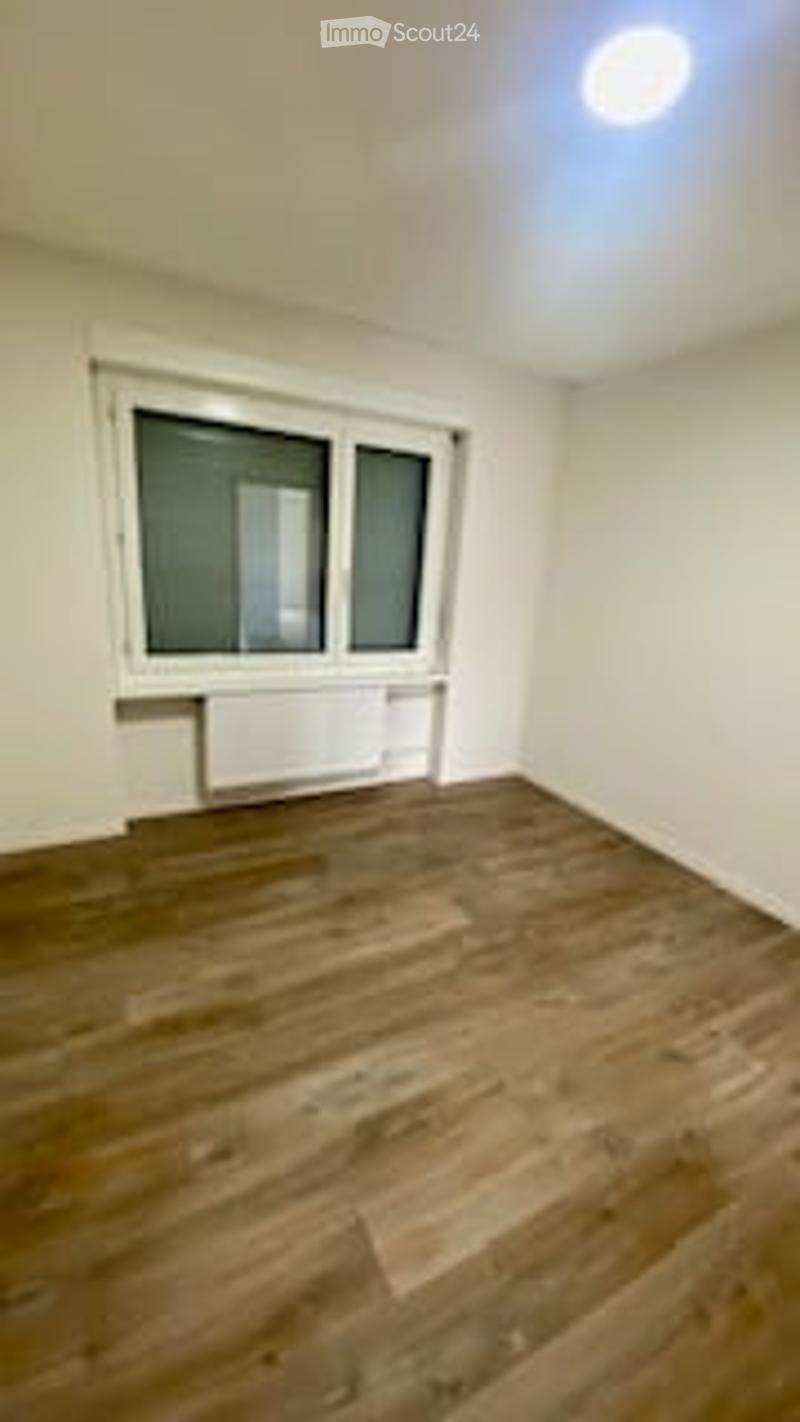 Completely empty room with wooden flooring, white walls, and a single window with white frame. No furniture or equipment present.