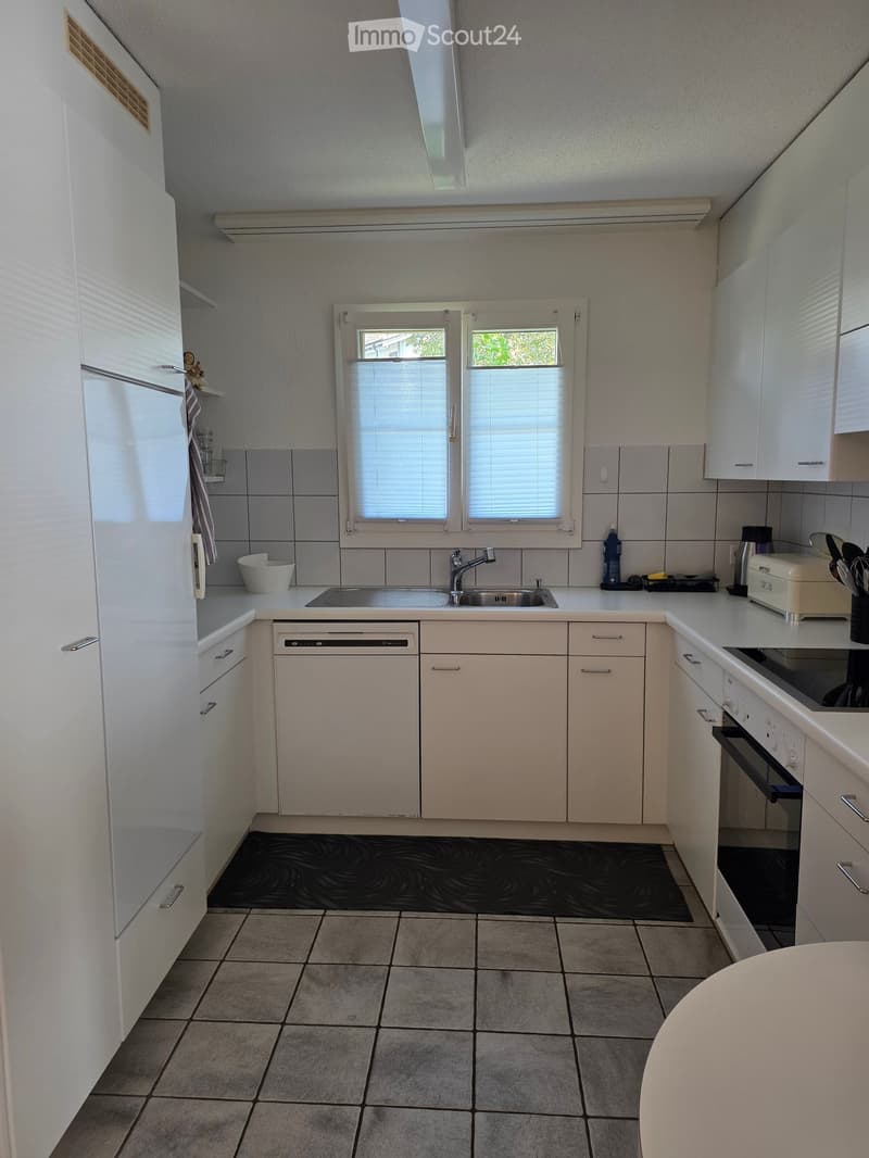 Modern kitchen with white cabinets, tiled walls, and a central island. Features include a sink, dishwasher, oven, and various appliances.