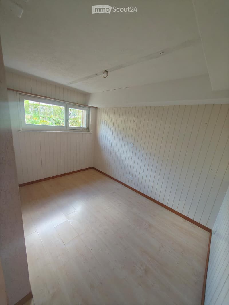 Empty room with wooden panel walls, light wooden floor, and a single window with white frame. No furniture or equipment present.