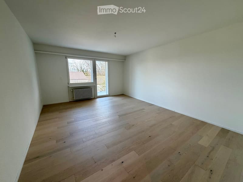 Empty room with wooden flooring, white walls, and a large window with a view of the outside.