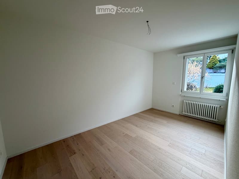 Empty room with wooden flooring, white walls, and a window with a radiator below it.