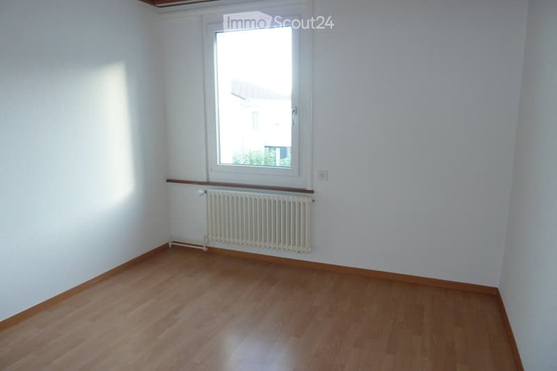 Empty room with wooden flooring, white walls, a window, and a radiator below the window.