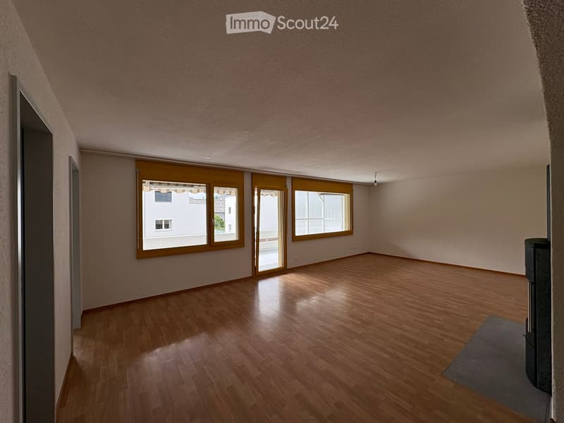 Empty room with wooden flooring, large windows, and sliding glass doors leading to a balcony.