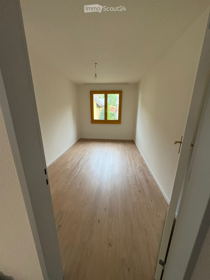 Empty hallway with wooden flooring, light-colored walls, and a single window with wooden frame. Natural light streams in from the window, illuminating the space.