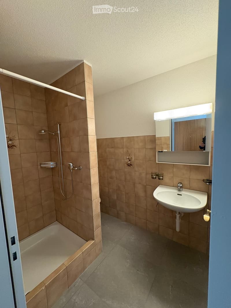 Bathroom with beige tiled walls, a corner shower, a white sink, and a mirror with built-in lighting.
