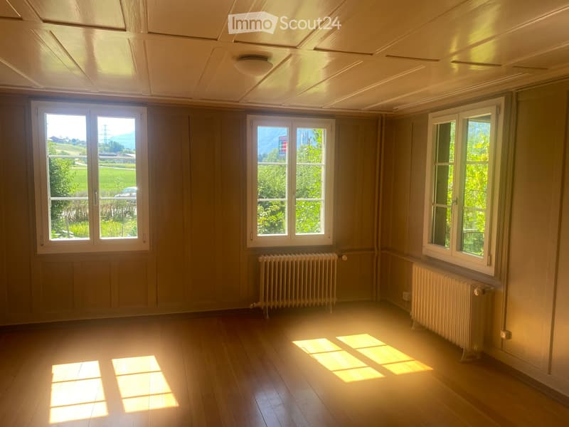 Empty room with wooden flooring, large windows, radiators, and natural light streaming in.