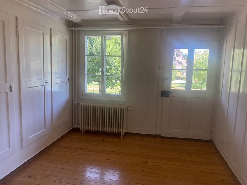 Empty room with wooden flooring, white walls, two doors, a window, and radiators.