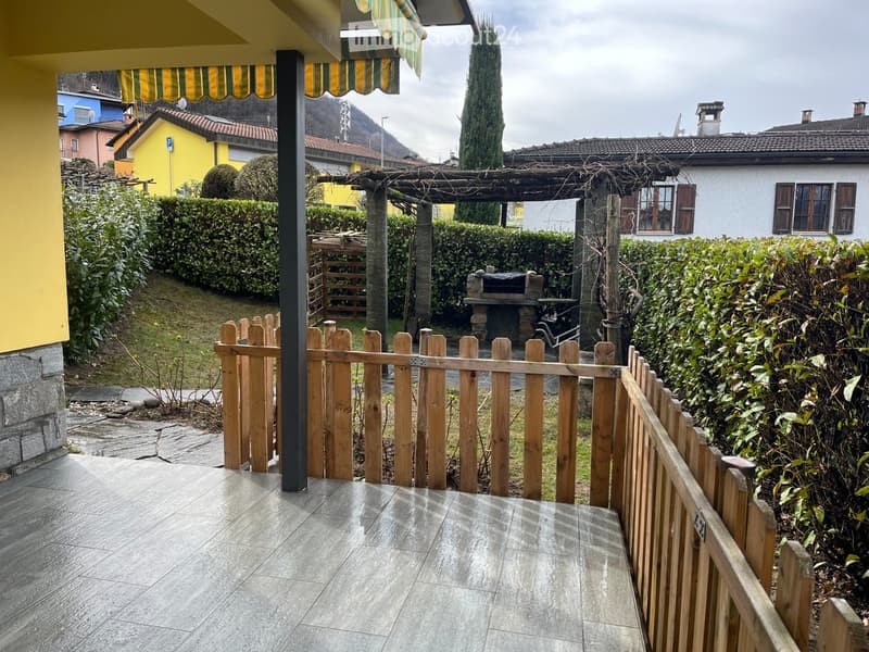 Balcony with tiled flooring, wooden fence, and view of a landscaped garden with a pergola, barbecue, and surrounding houses.