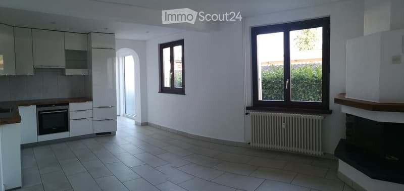 Modern kitchen with white cabinets, stainless steel appliances, tiled floor, and large windows. Features a built-in oven, refrigerator, and radiator under the windows.