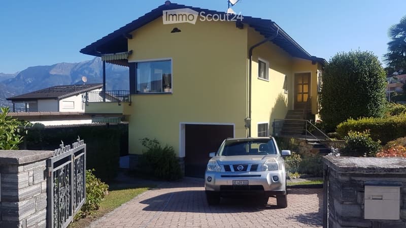 Two-story yellow house with a garage, balcony, and scenic mountain view in the background. A silver SUV is parked in the driveway.