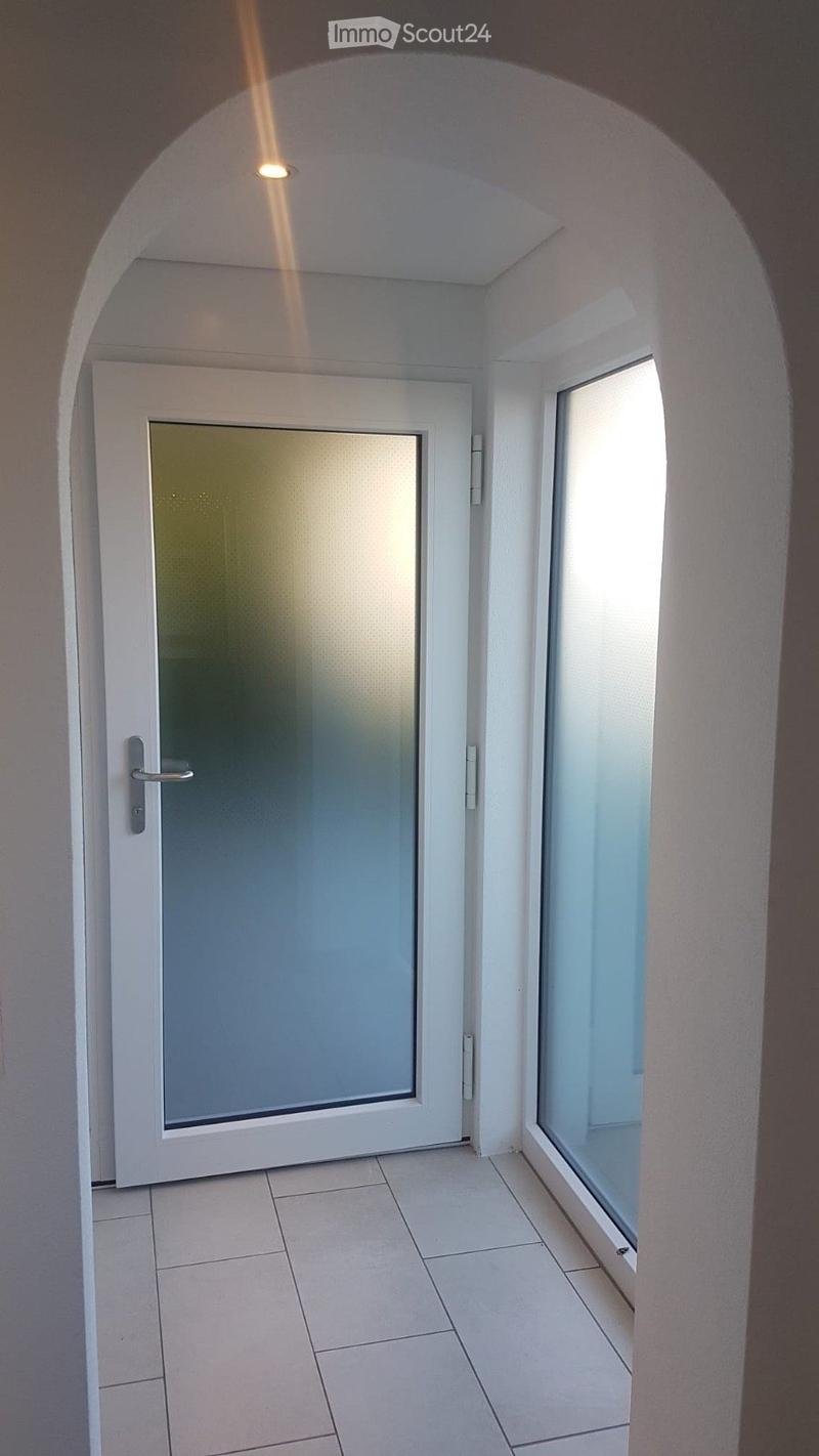 Empty hallway with white tiled floor, white walls, a frosted glass door, and a small window allowing natural light.