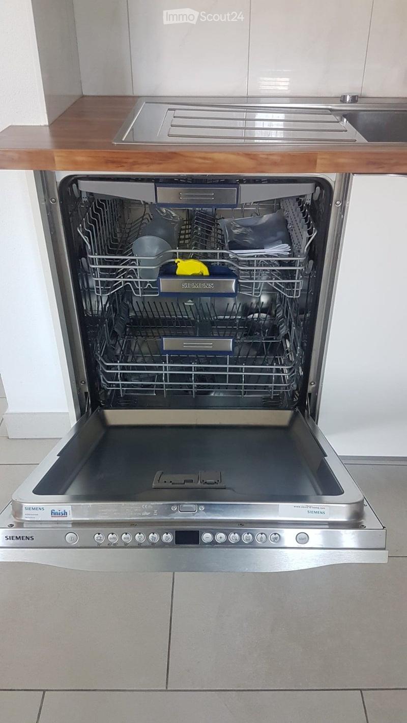 A modern kitchen featuring a Siemens dishwasher with an open door, revealing multiple racks and a wooden countertop above.