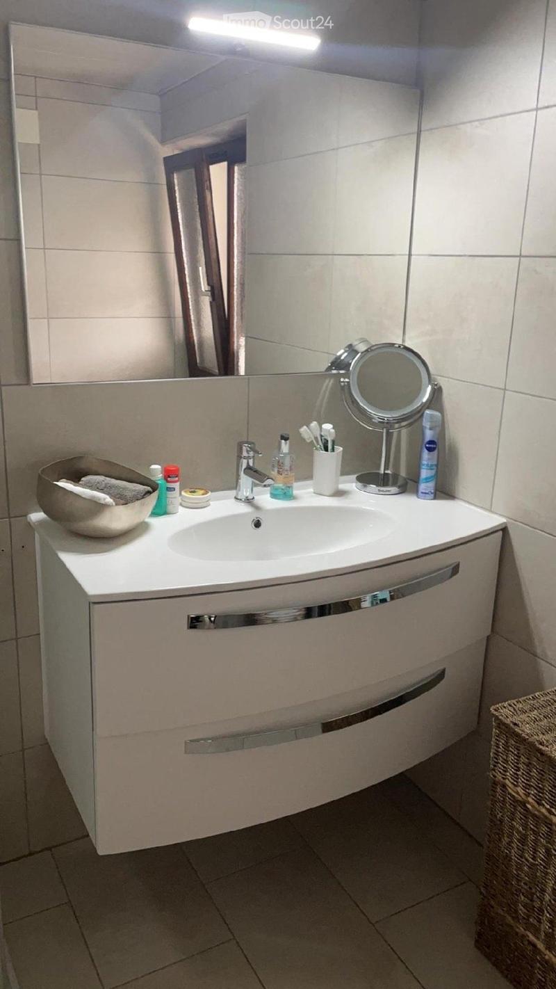 Modern bathroom with a white vanity cabinet, sink, mirror, and various toiletries including a toothbrush holder, cosmetic bottle, and a bowl on the counter.